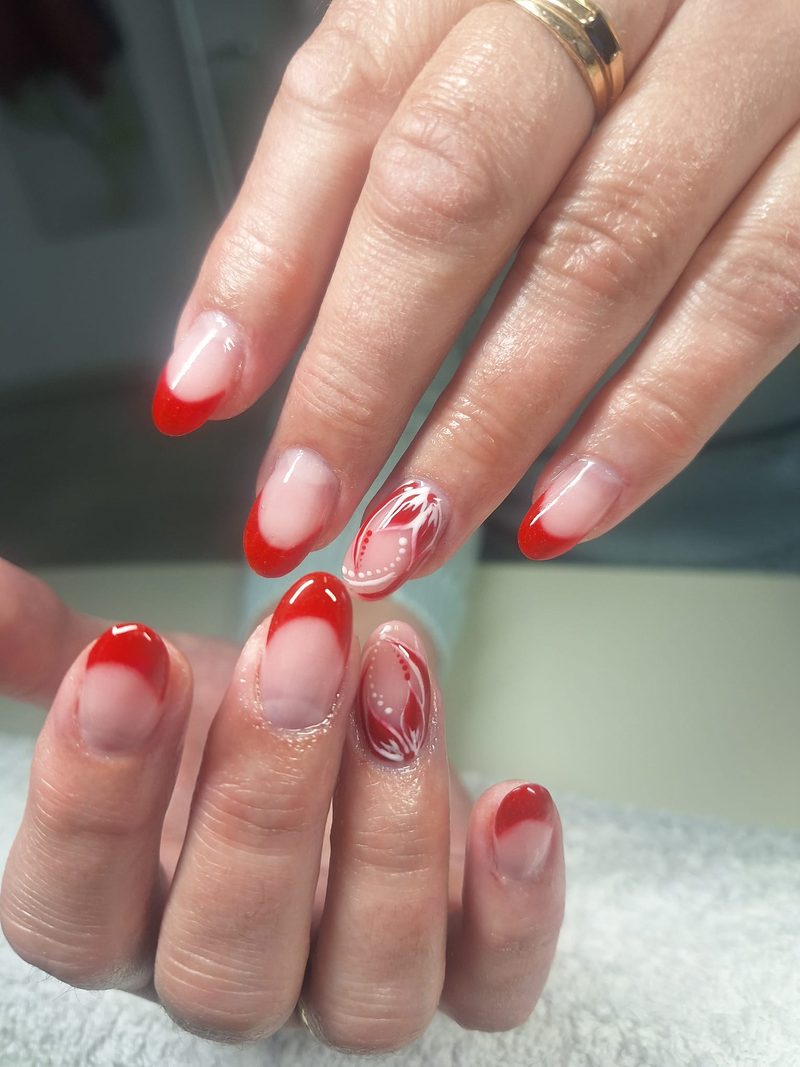 Mandelförmige Nägel mit roter French und weißer Blumenmalerei auf dem Ringfinger