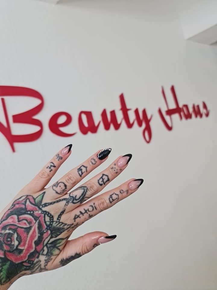 Spitze Nägel mit schwarzer French und Strasssteinen vor dem Beauty-Haus-Schriftzug im Studio