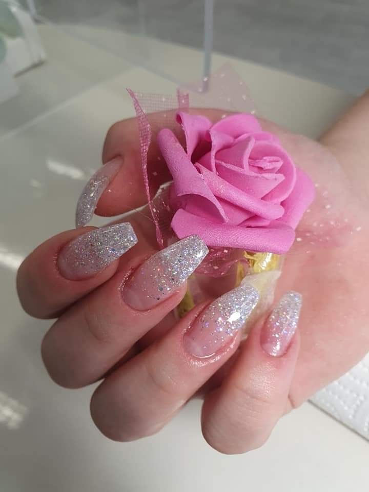Lange Nägel mit silbernem Glitzerverlauf, die Hand hält eine rosa Rose
